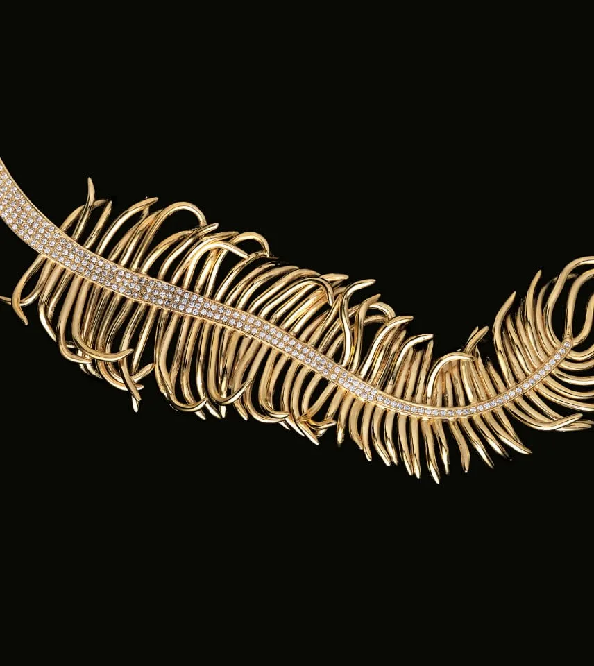 Detail of a yellow gold piece of jewellery in the shape of a palm leaf, with multiple rows of diamonds along the central rib.