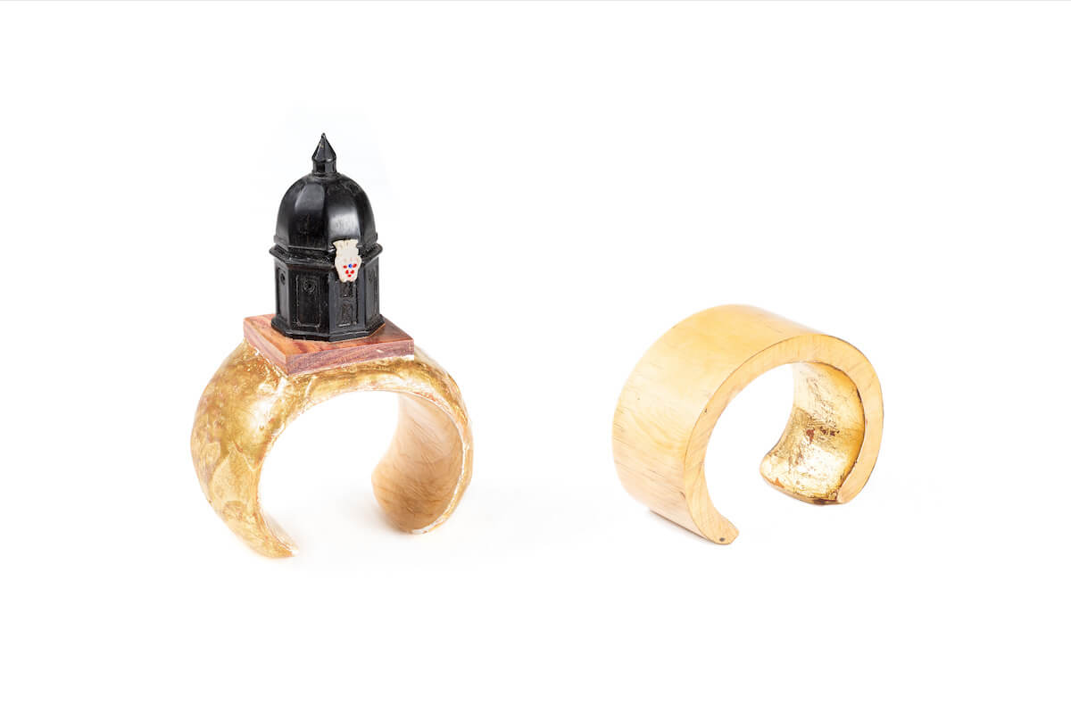 Due bracciali rigidi martellati dorati; su uno è montata una miniatura architettonica nera a cupola.