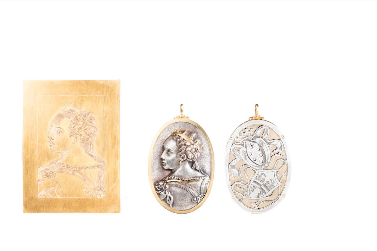 Piastra incisa in metallo dorato e due pendenti ovali bicolore: profilo femminile coronato sul fronte e motivo araldico traforato sul retro.